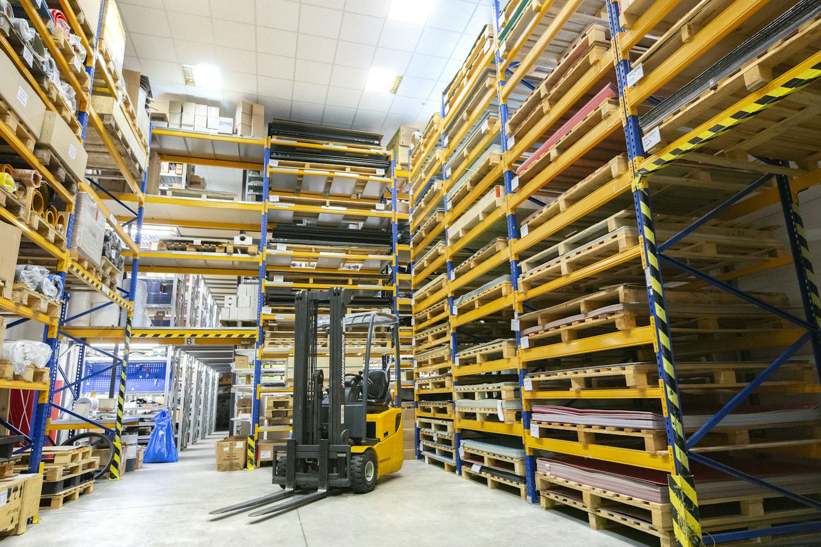 Warehouse racking loaded with pallets and a forklift